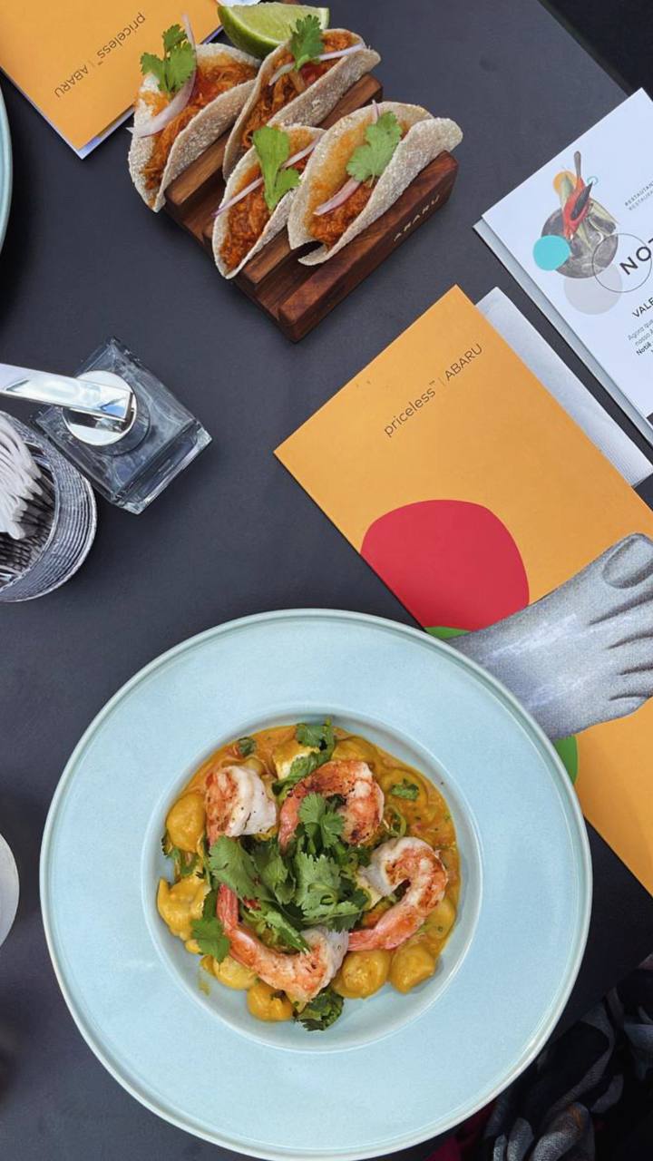 Flatlay com tacos, camarão em molho dourado e menus em ambiente sofisticado